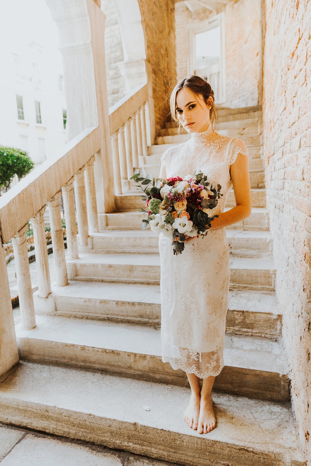 Barefoot bride with bouquet on stone steps outdoor