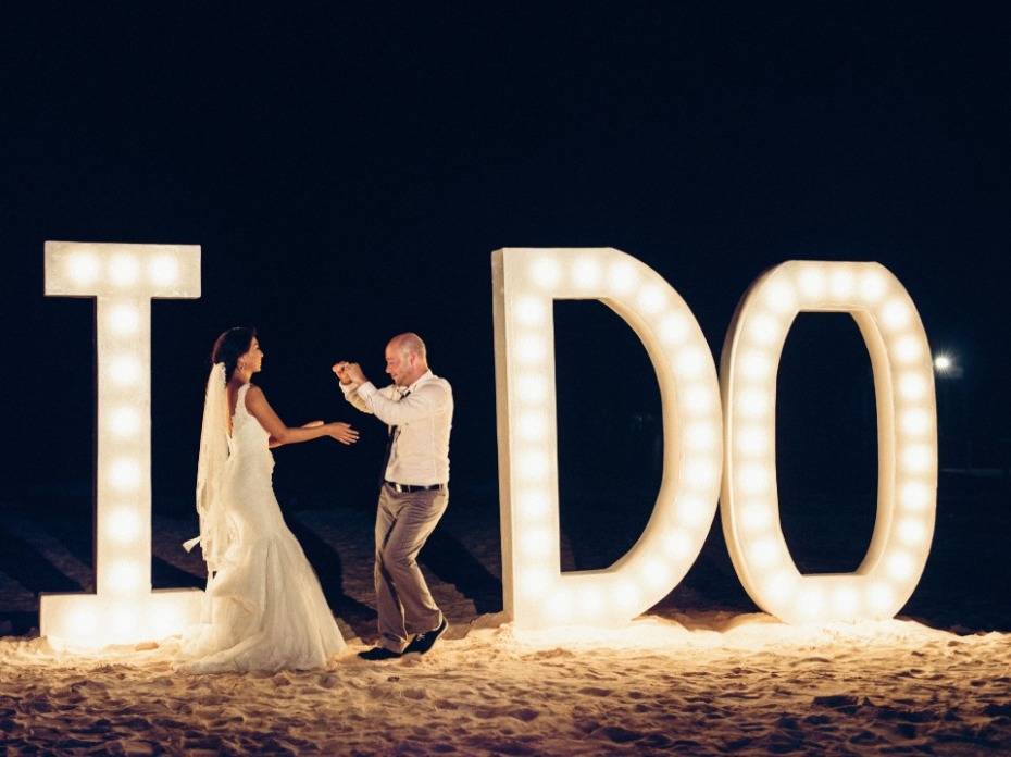 Couple celebrating wedding with I DO sign lit up on beach