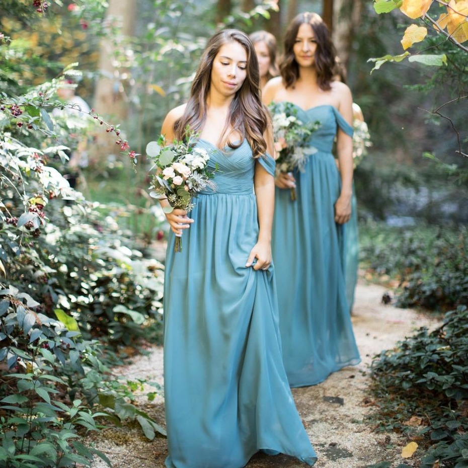 Bridesmaids in blue dresses carry bouquets outdoors