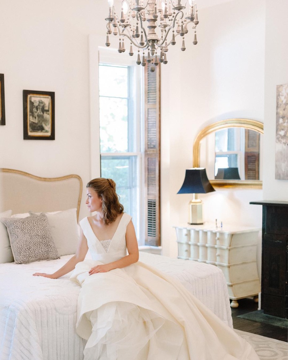 Bride in wedding dress sitting on elegant bedroom bed