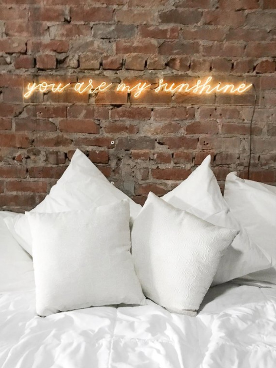 Cozy bed with pillows and a you are my sunshine neon sign