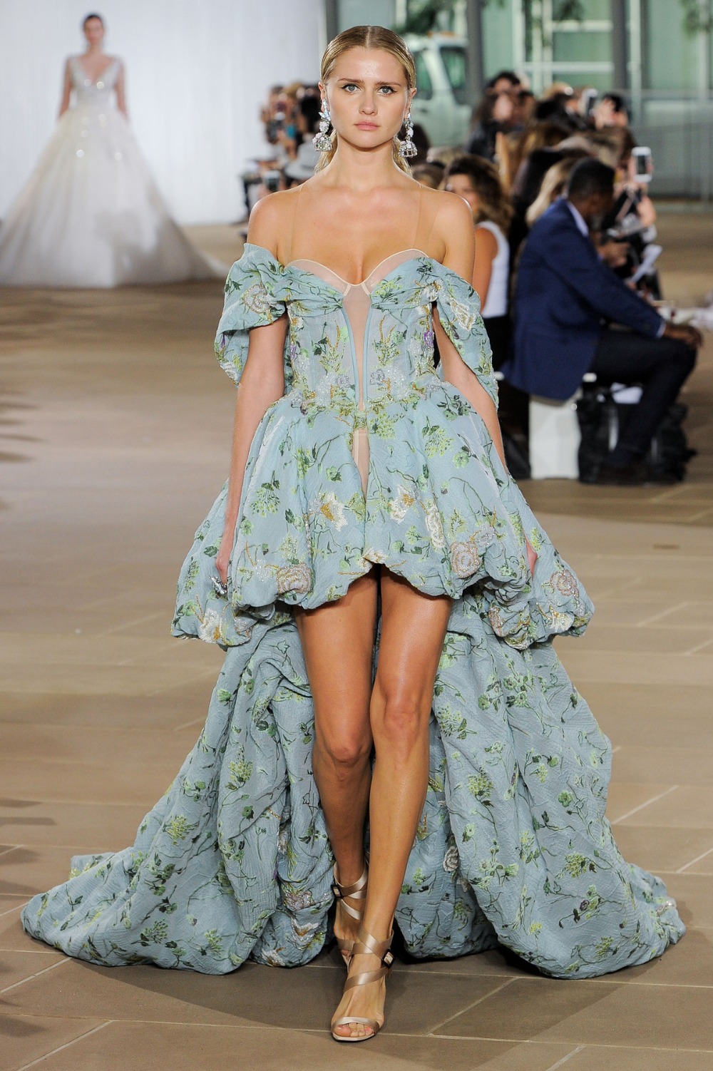 Woman modeling a short floral dress with a long train at a fashion show
