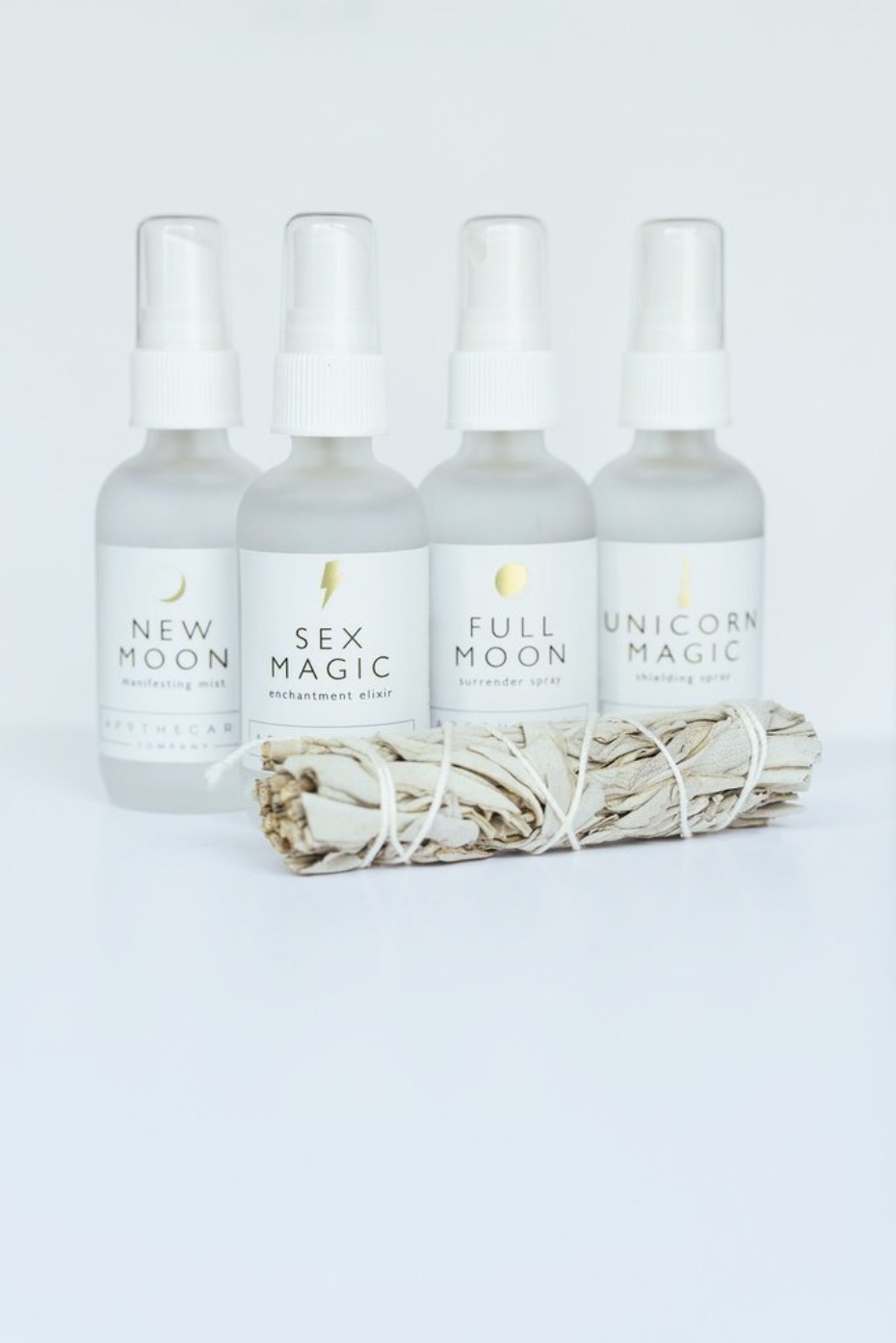Four magic mist bottles with sage bundle on a white surface
