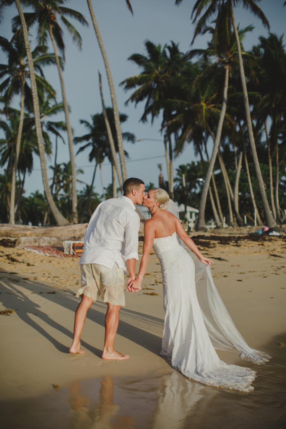 Couple kissing on a beach with palm trees, wedding day