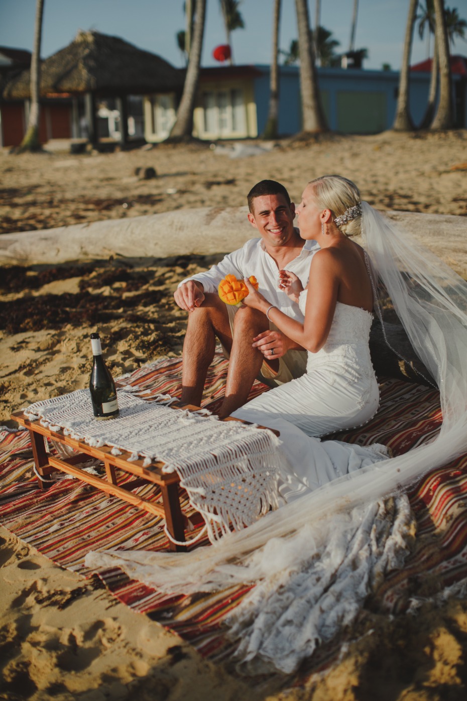 Newlyweds enjoy a romantic beach picnic with champagne and fruit