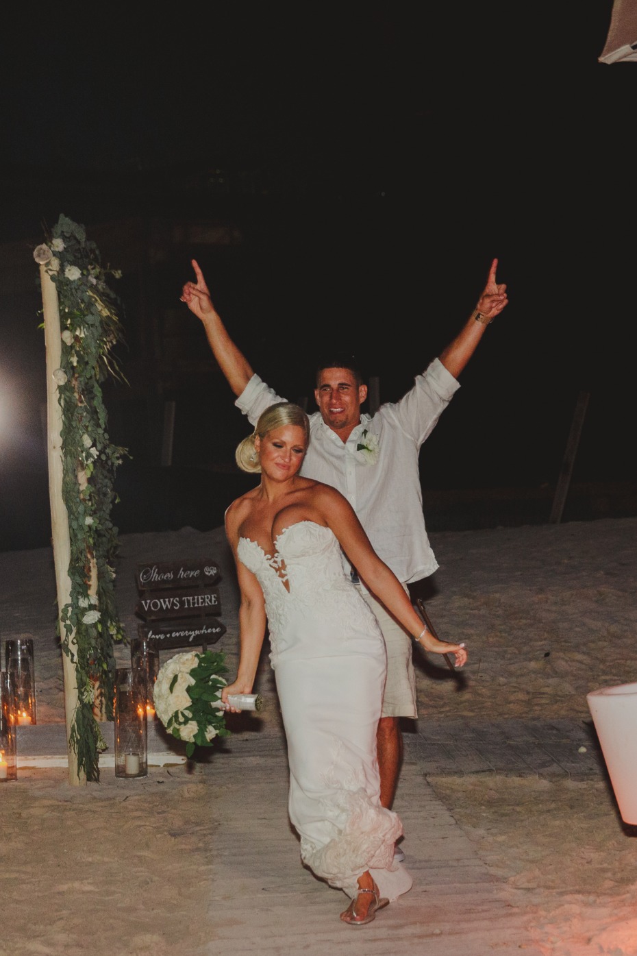 Newlyweds celebrate after a beach wedding at night with arms raised
