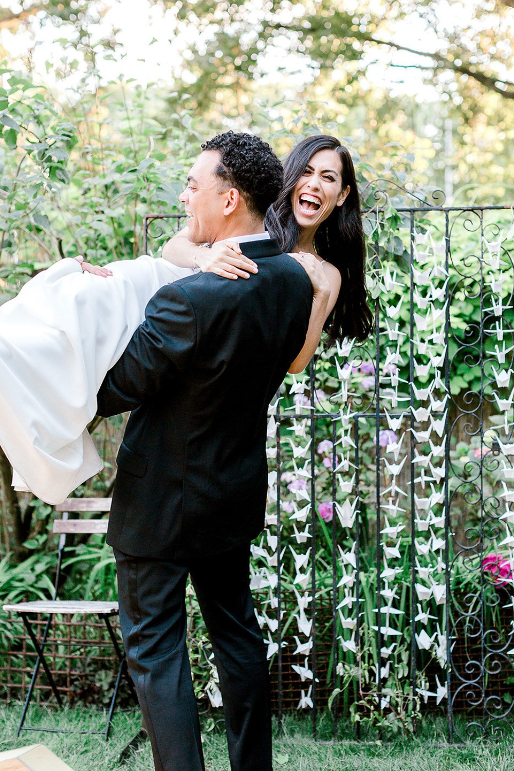 Groom carrying joyful bride at outdoor wedding ceremony with crane decor