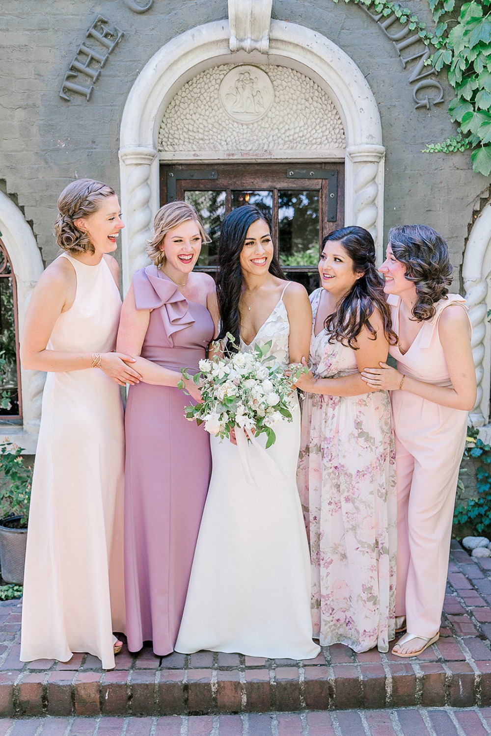 Bride and bridesmaids in pastel dresses smiling outdoors