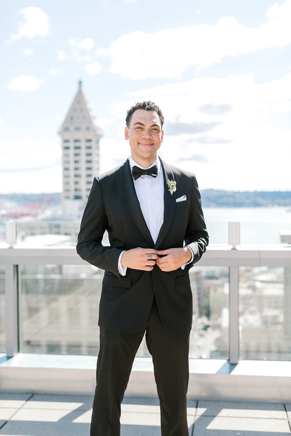 Smiling groom in a black tuxedo on a rooftop with city view