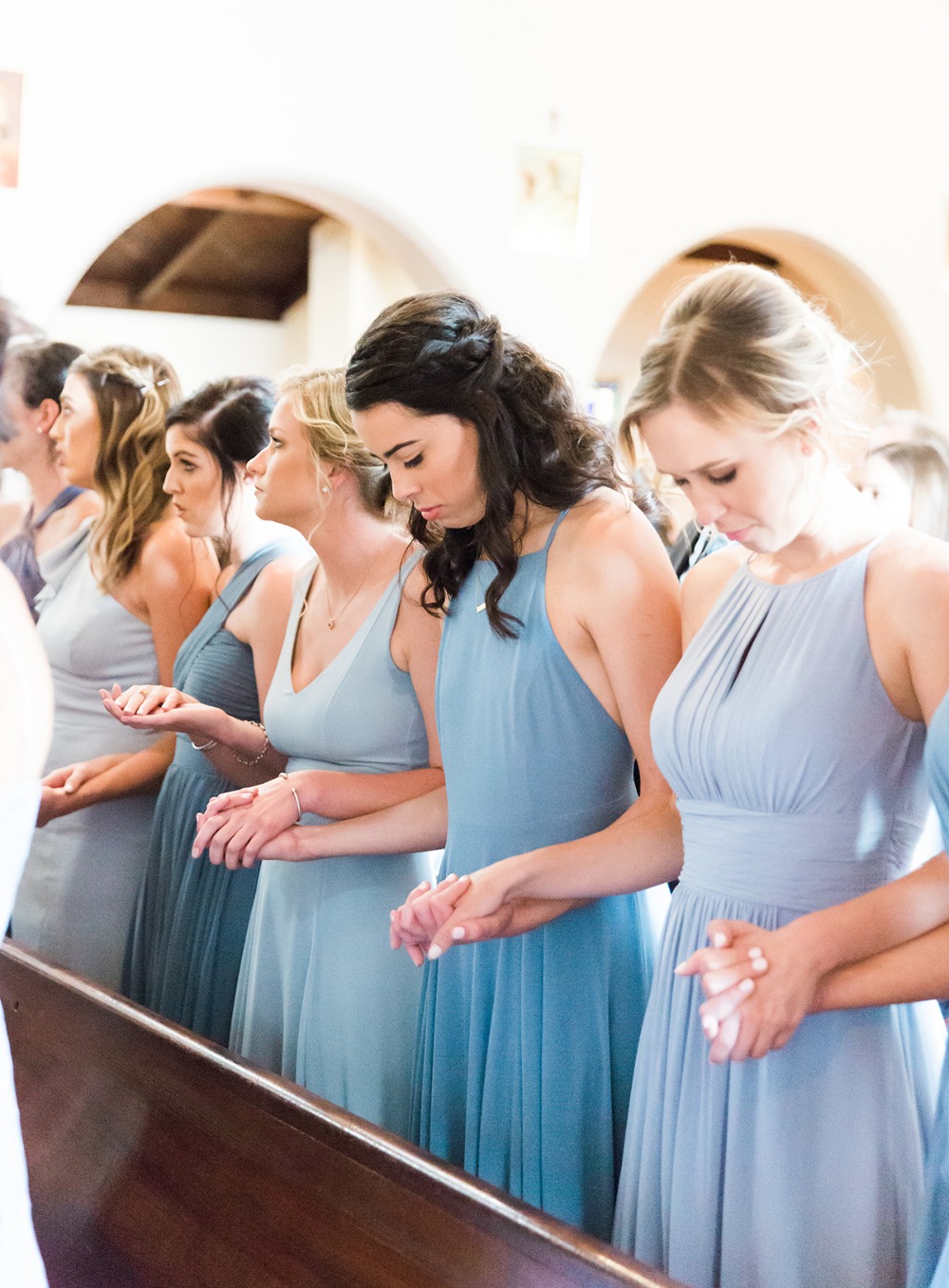 Bridesmaids holding hands and praying during a wedding ceremony