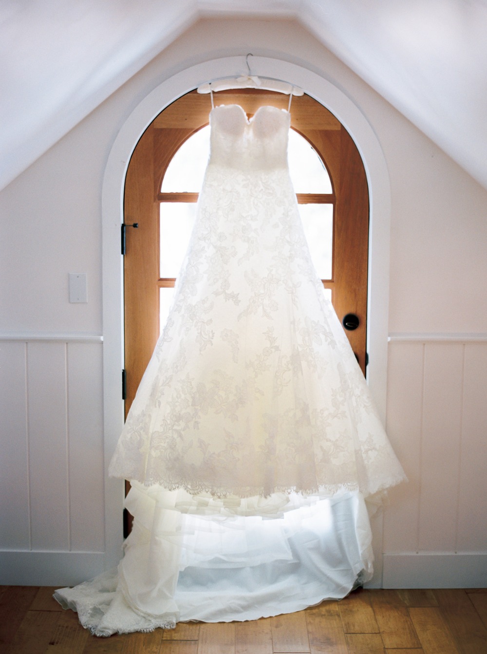 Lace wedding gown hangs on a wooden arched doorway