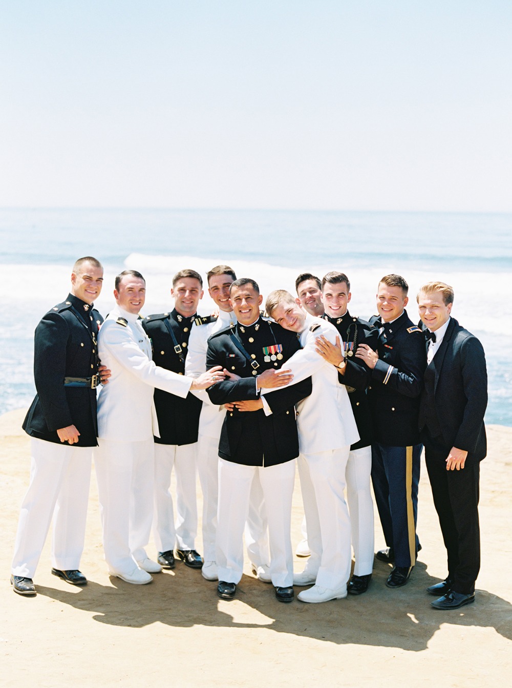 Groomsmen in military uniforms pose near the ocean for a wedding