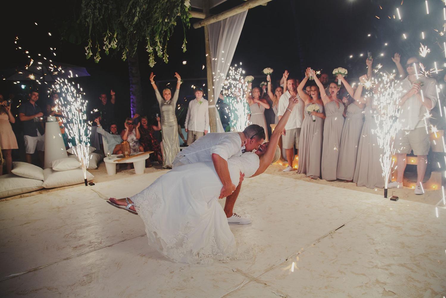Bride and groom share a kiss as wedding guests celebrate with fireworks
