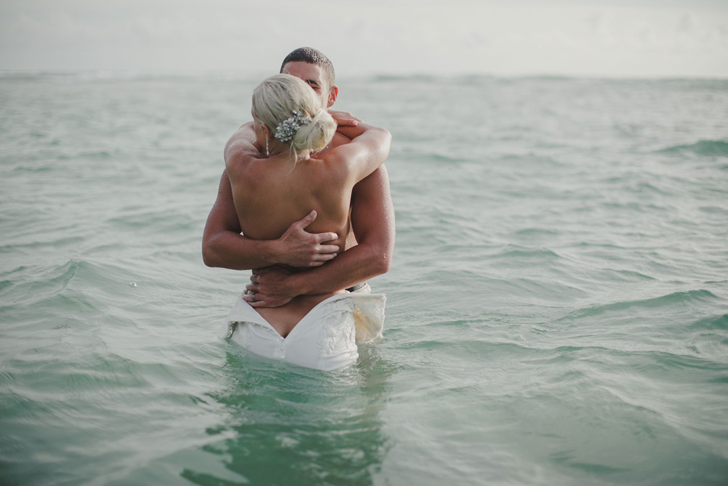 Romantic couple embracing in the sea during their wedding day