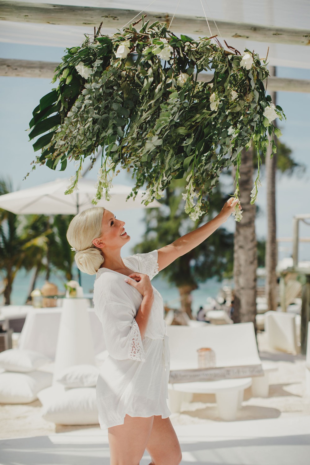 Woman touching a floral arrangement under a beach venue