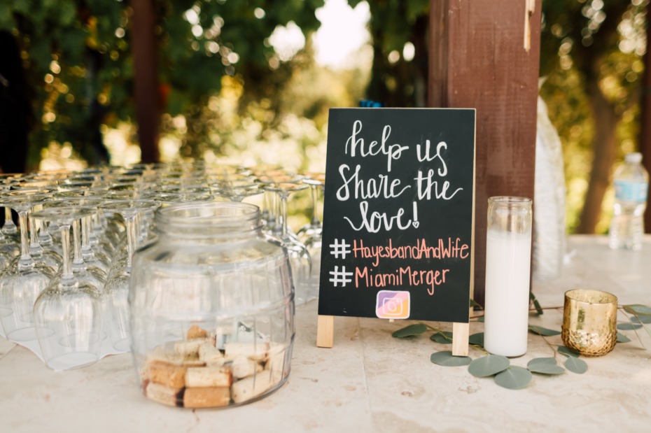 Wedding hashtag sign with wine glasses and cork jar