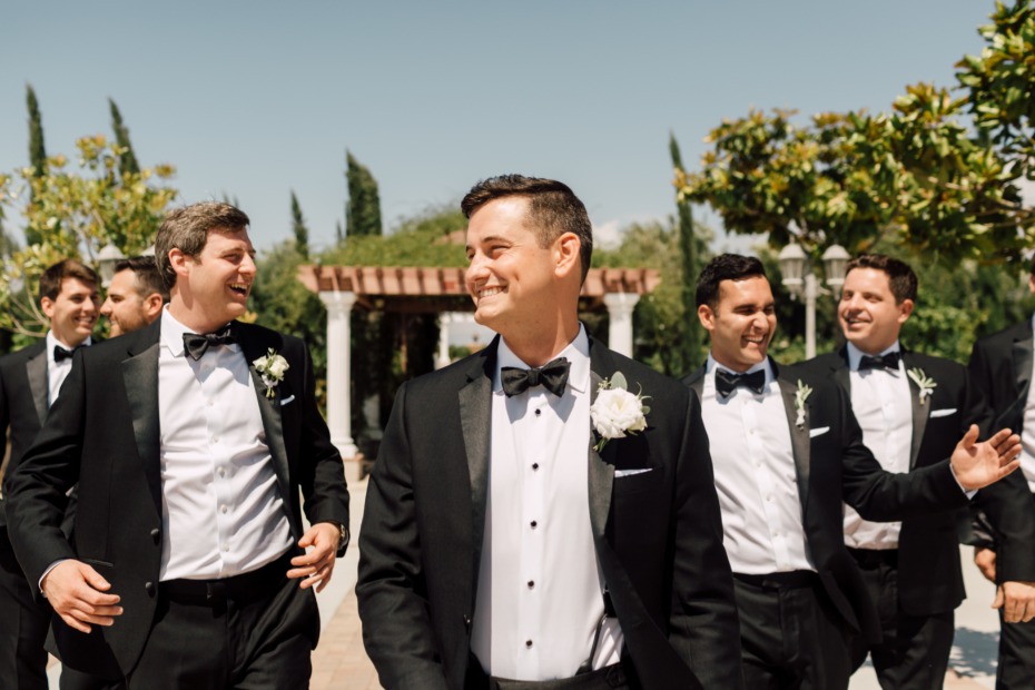 Groomsmen in tuxedos smiling at an outdoor wedding