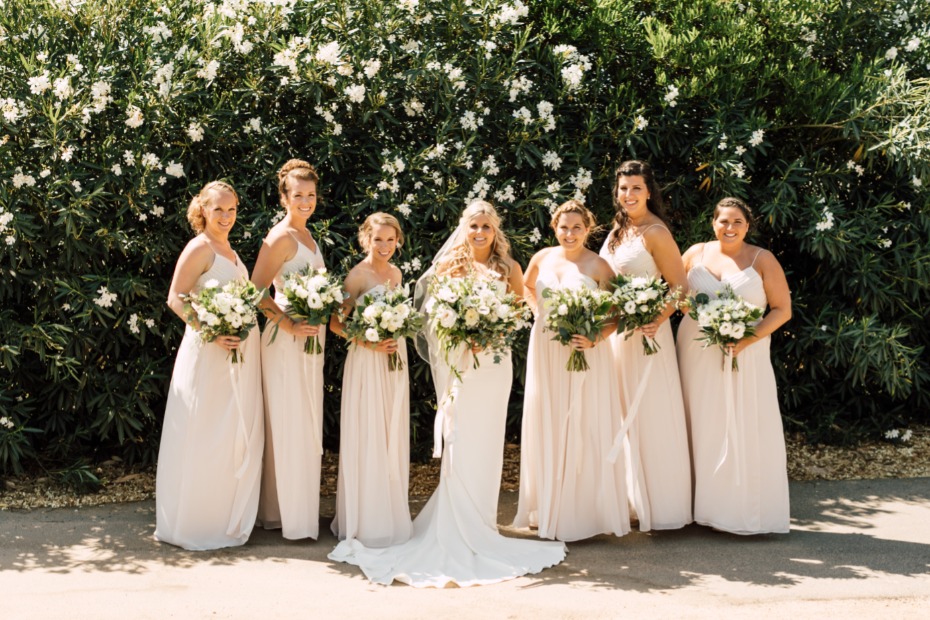 Bride and bridesmaids pose with white flowers outdoor