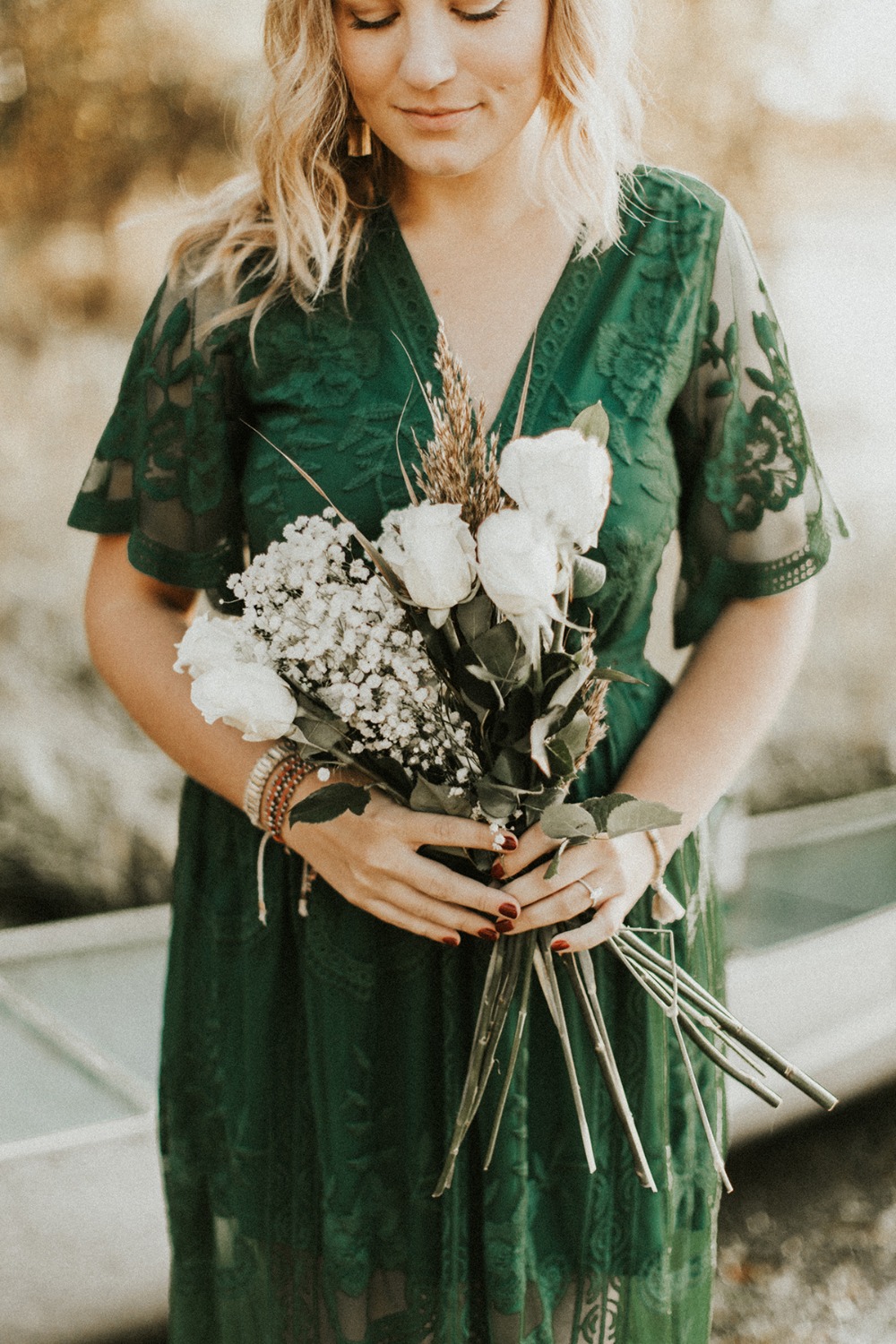 Blond woman in green dress holding white flower bouquet outdoor