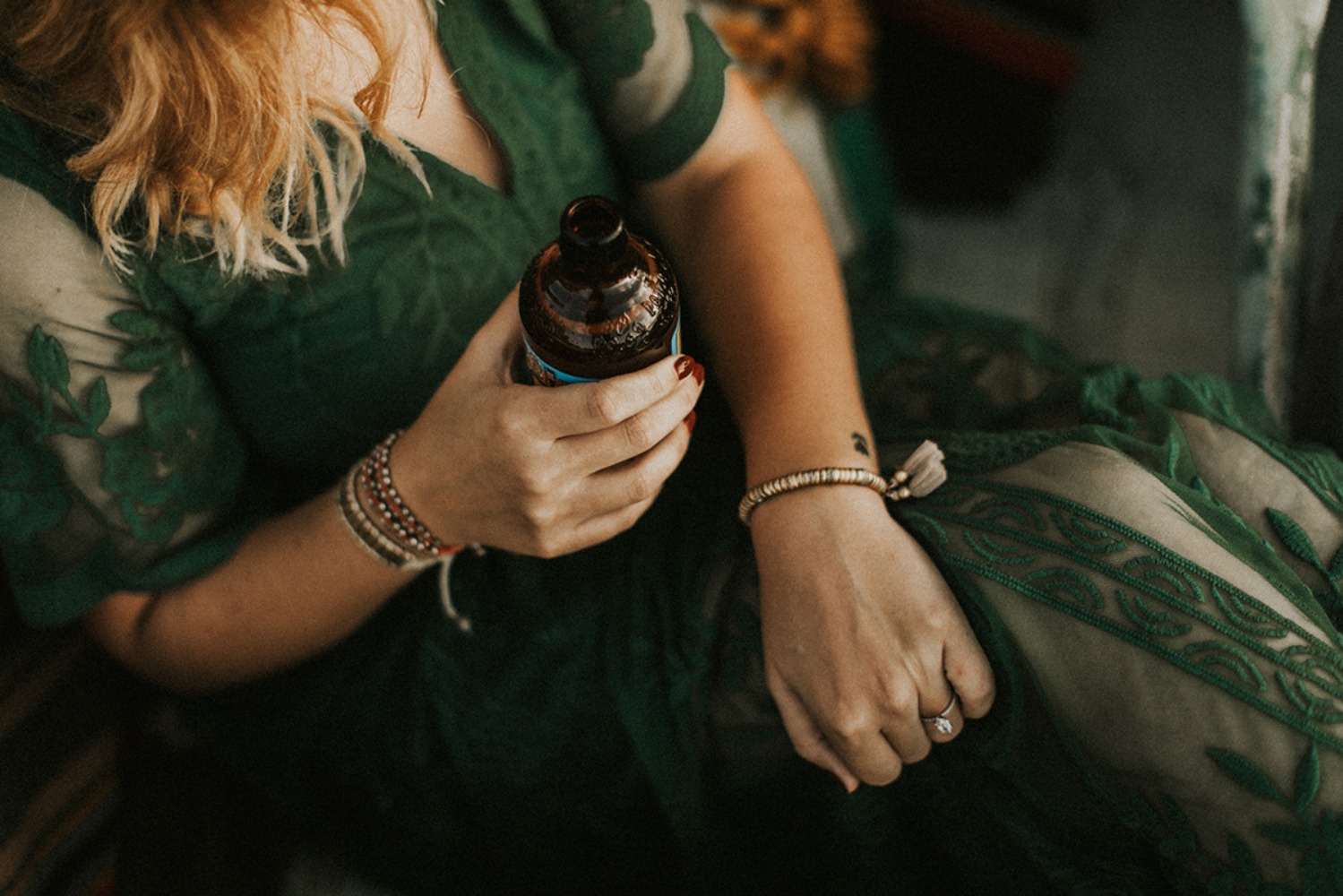 Woman in green lace dress and bracelets holds drink bottle