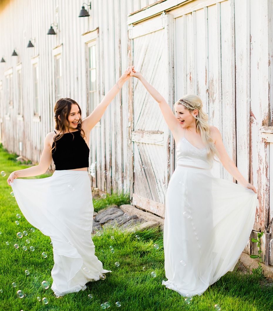 Two women in white dresses joyfully twirling outdoors