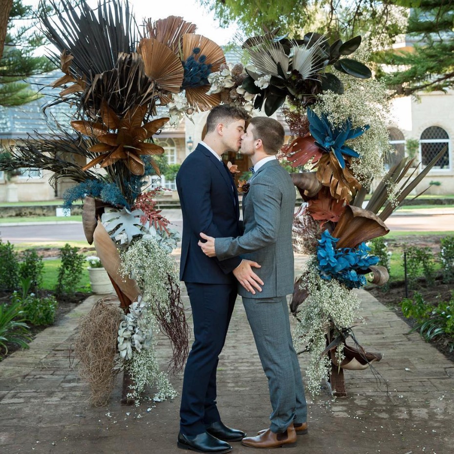 Grooms embracing in front of ceremony arch - @theflowergirlperth