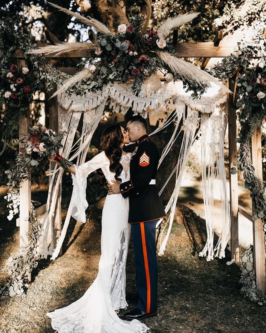 Marine groom and bride kissing at bohemian wedding altar
