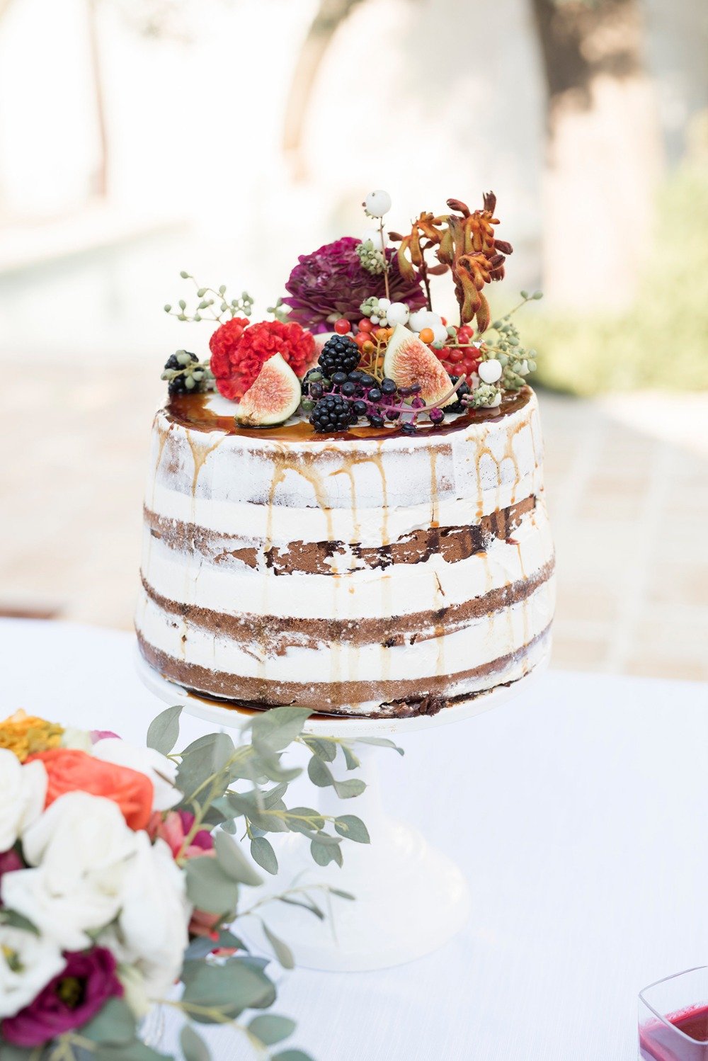 nearly naked wedding cake with fruit and floral top