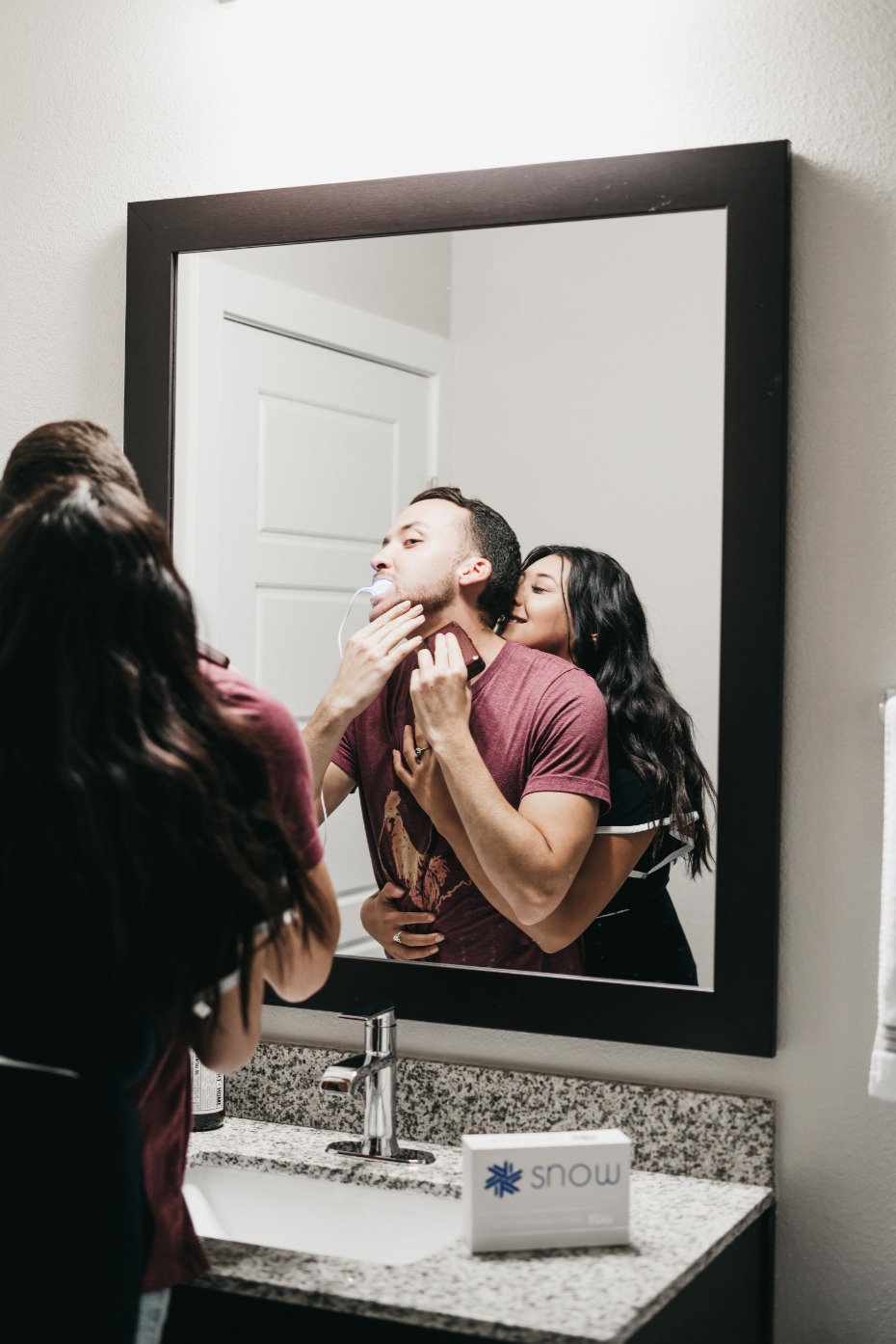 Snow Teeth Whitening Couple Embracing at the Bathroom Mirror He's Multitasking