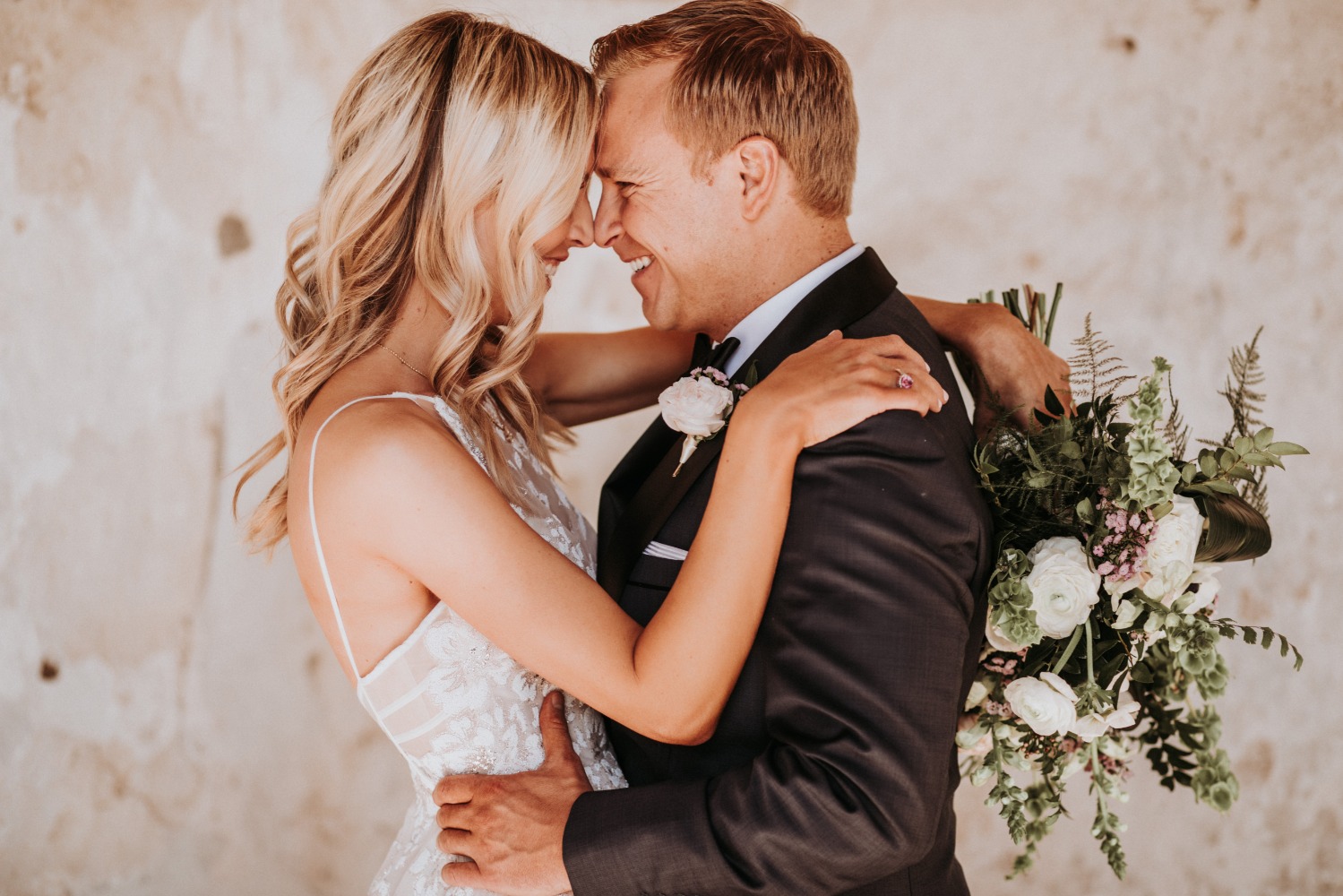 Smiling couple embraces on their wedding day holding bouquet