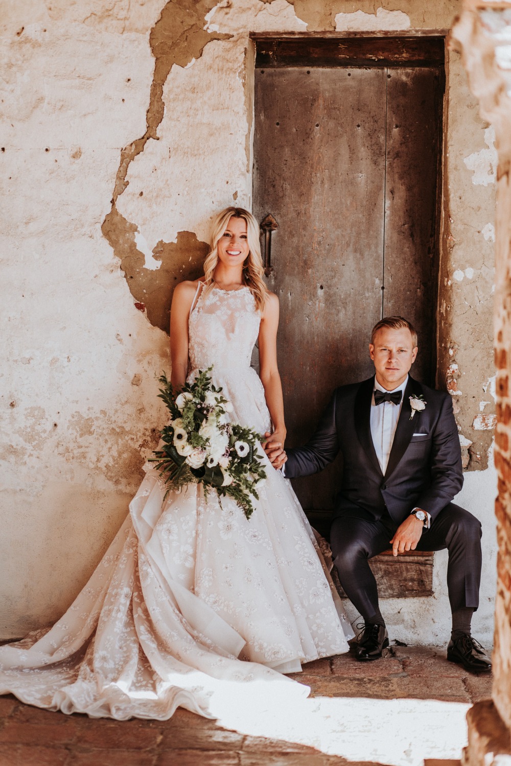 Bride and groom pose by an old building on their wedding day