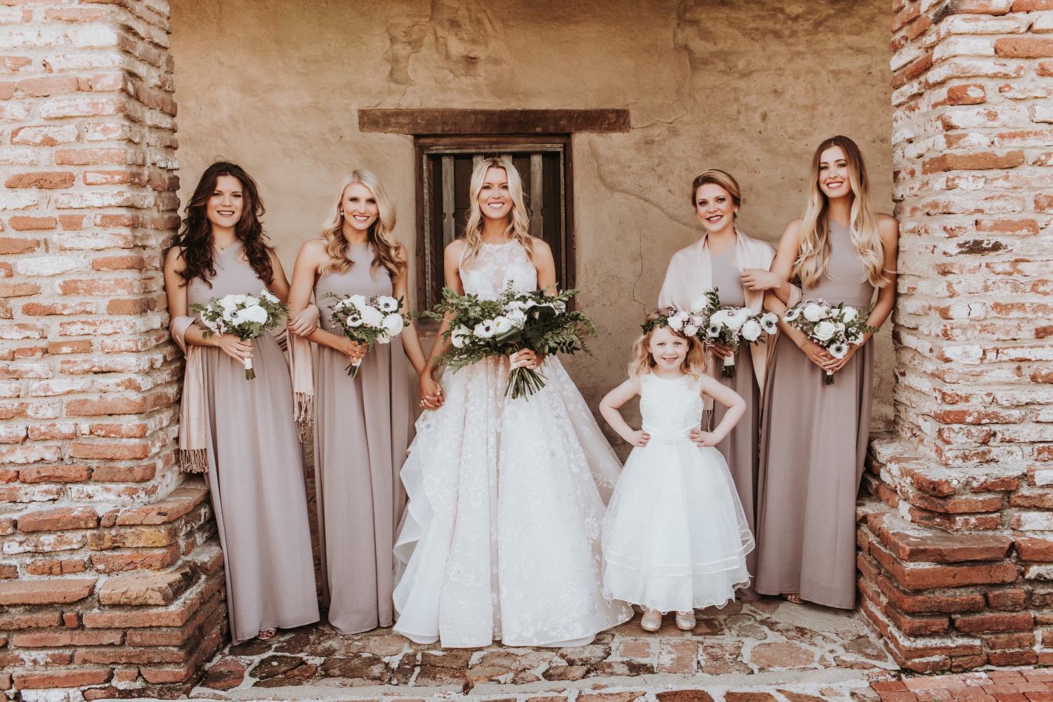 Bride and bridesmaids pose for a wedding photo near old brick wall