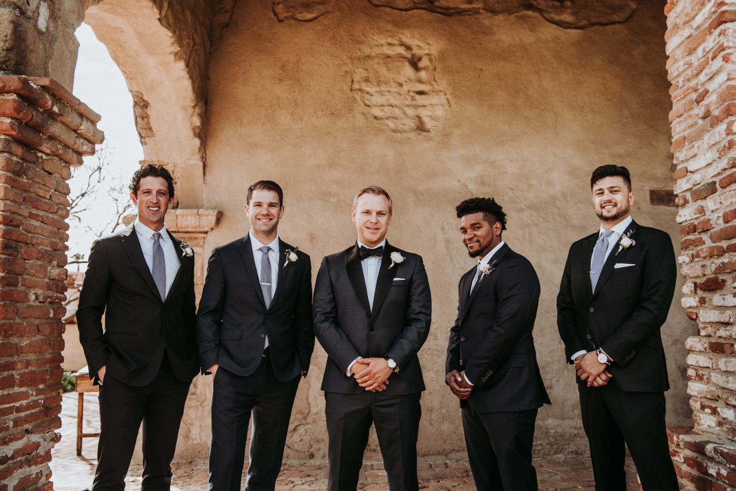 Group of groomsmen pose in front of a rustic stone wall for a wedding