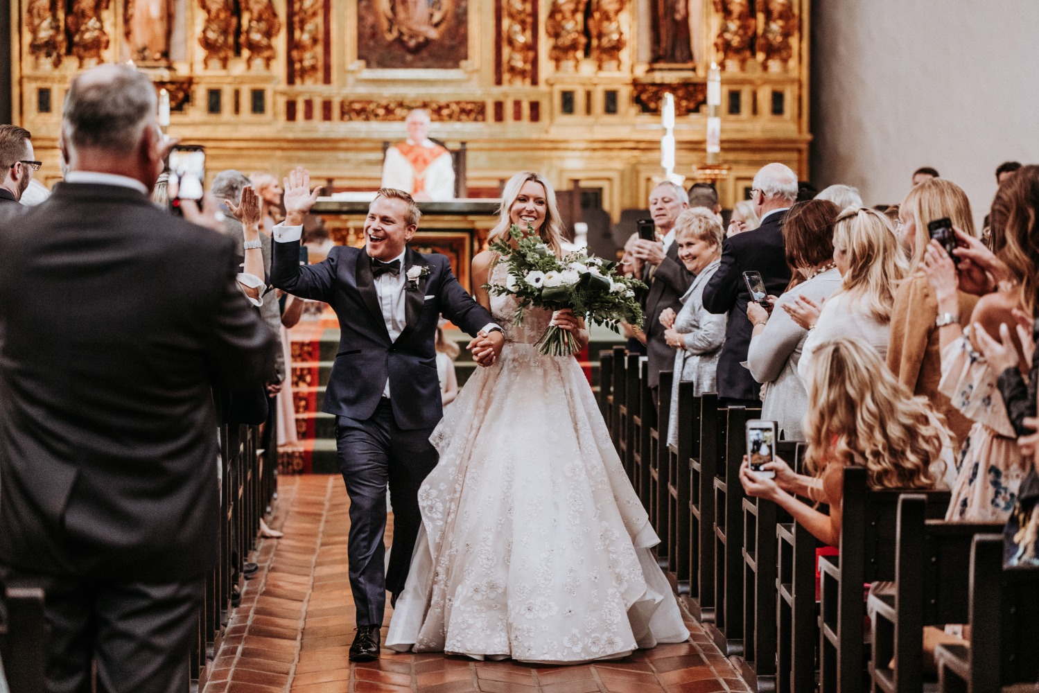 Newlyweds wave to guests during church wedding recessional