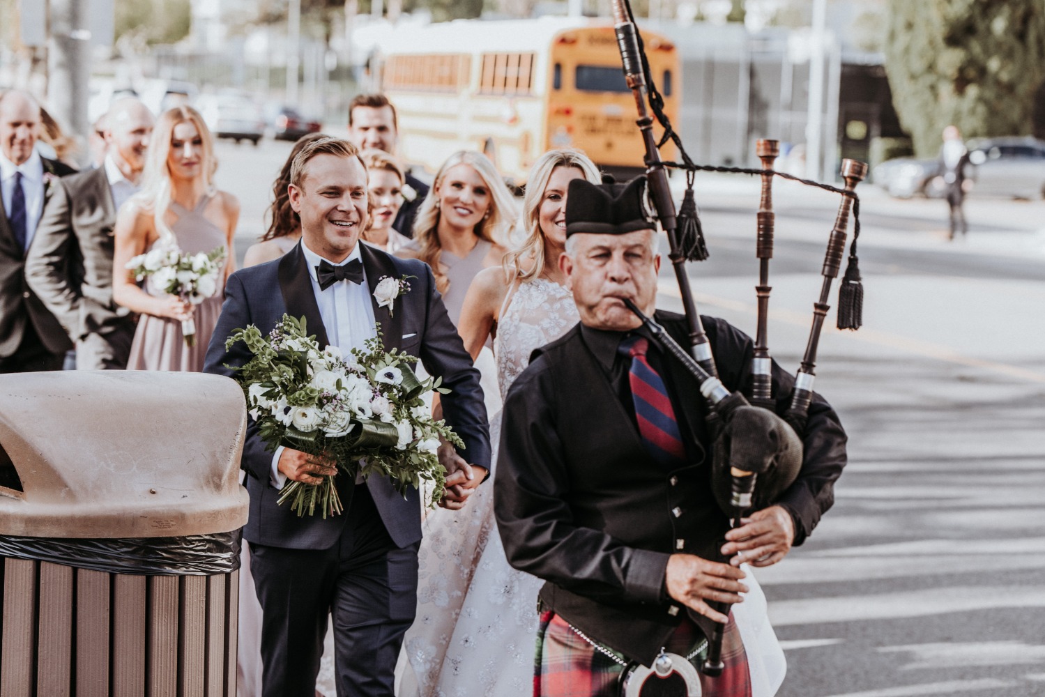 Groom leads wedding party with bagpiper on city street