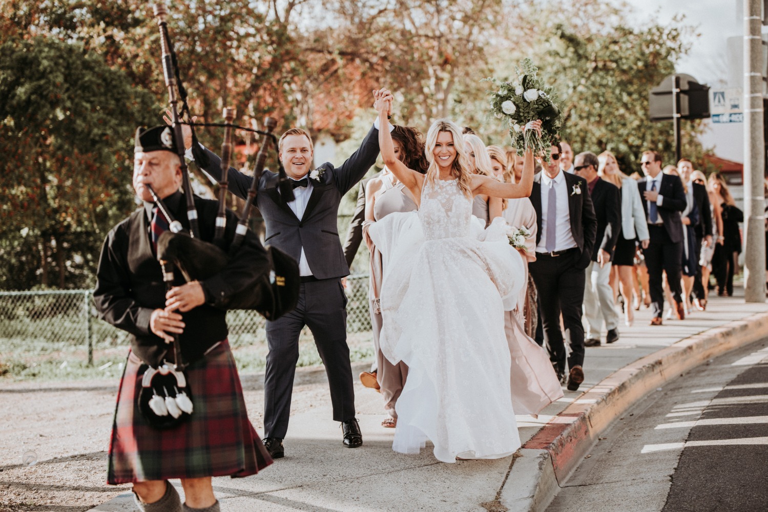 Happy bride groom and bagpiper lead wedding parade