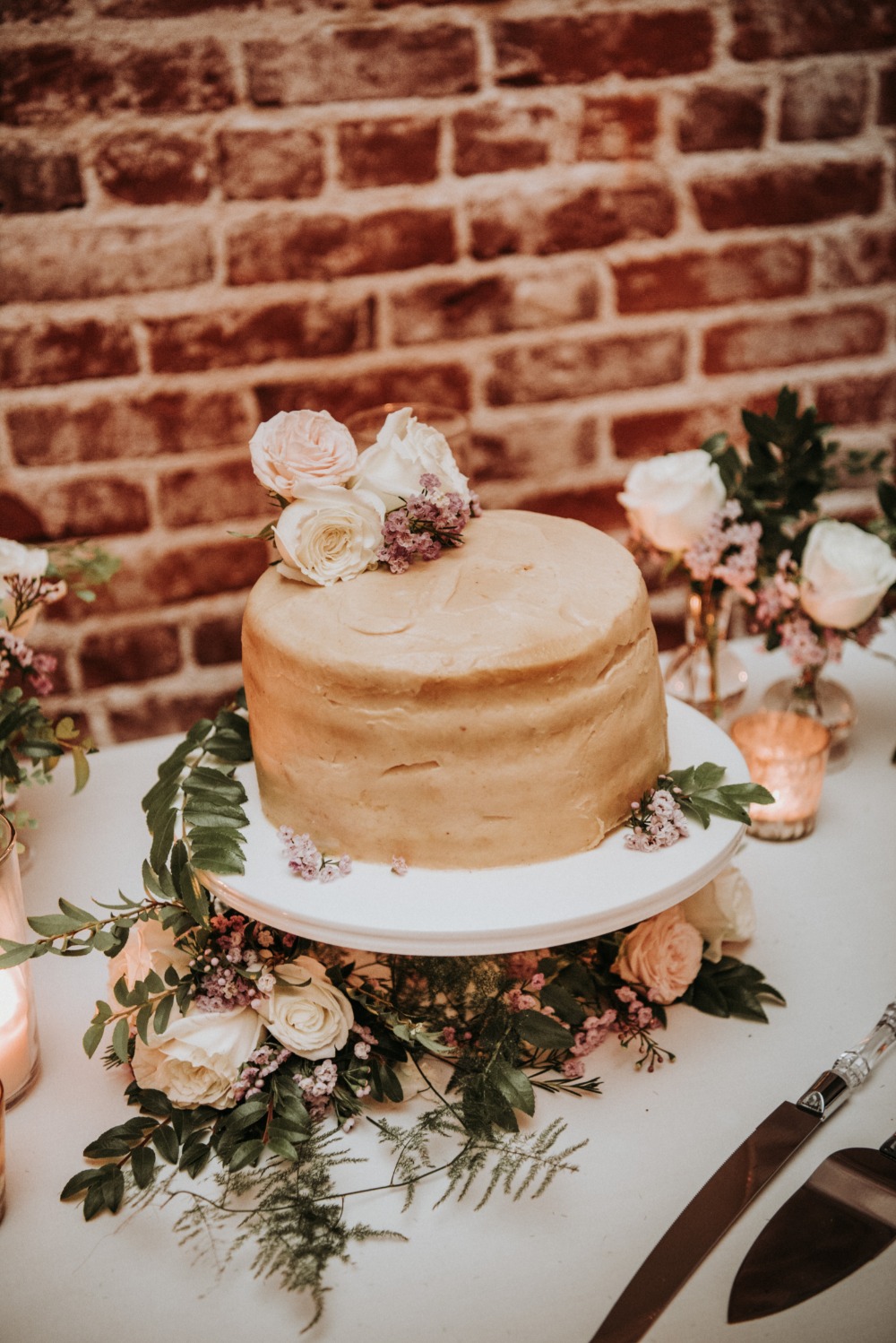 Wedding cake decorated with roses and greenery, brick background