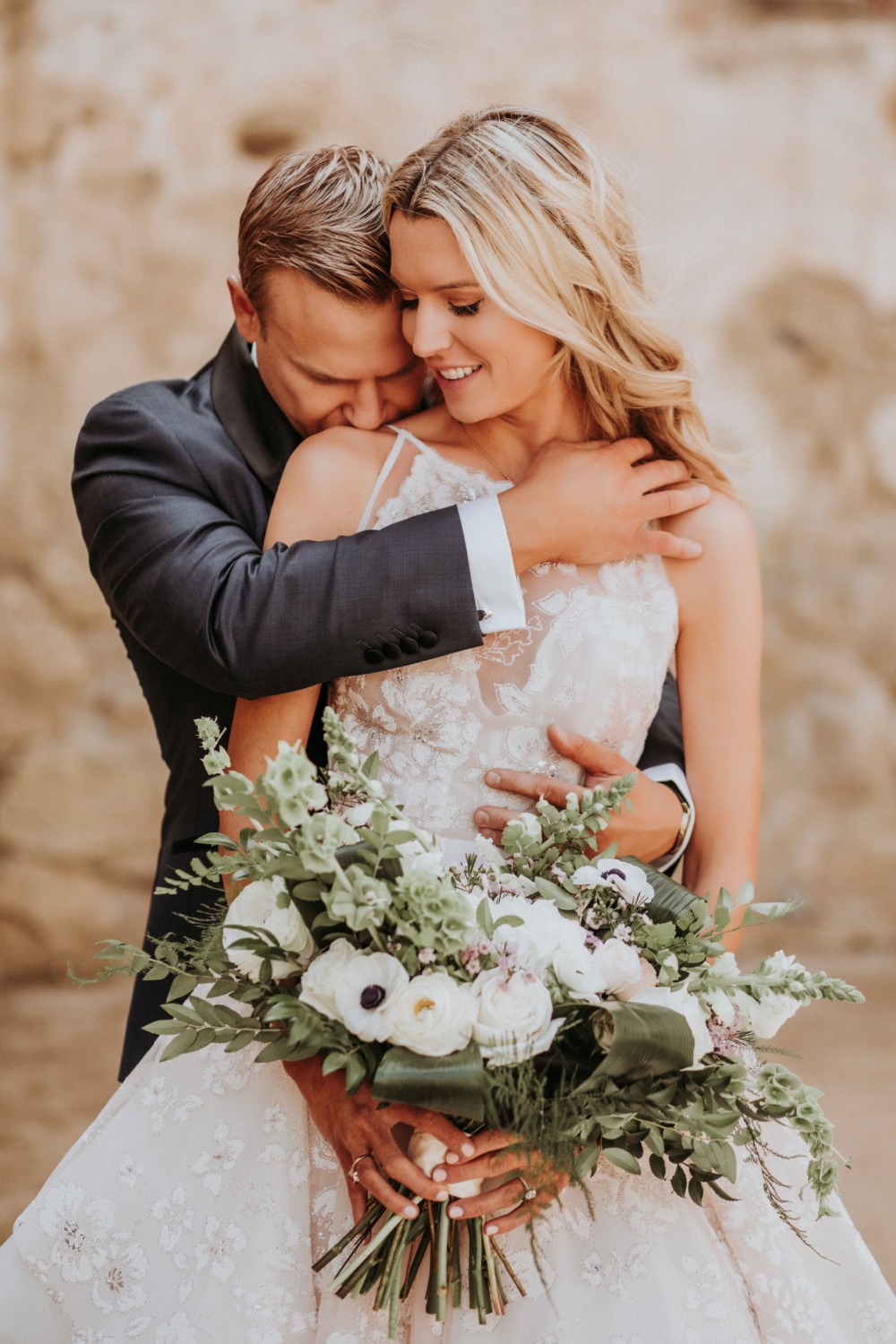 Happy bride and groom embrace, holding wedding bouquet