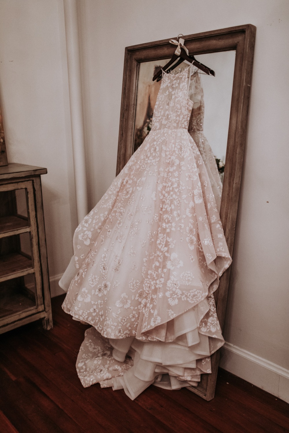 Elegant floral wedding dress displayed next to a rustic mirror