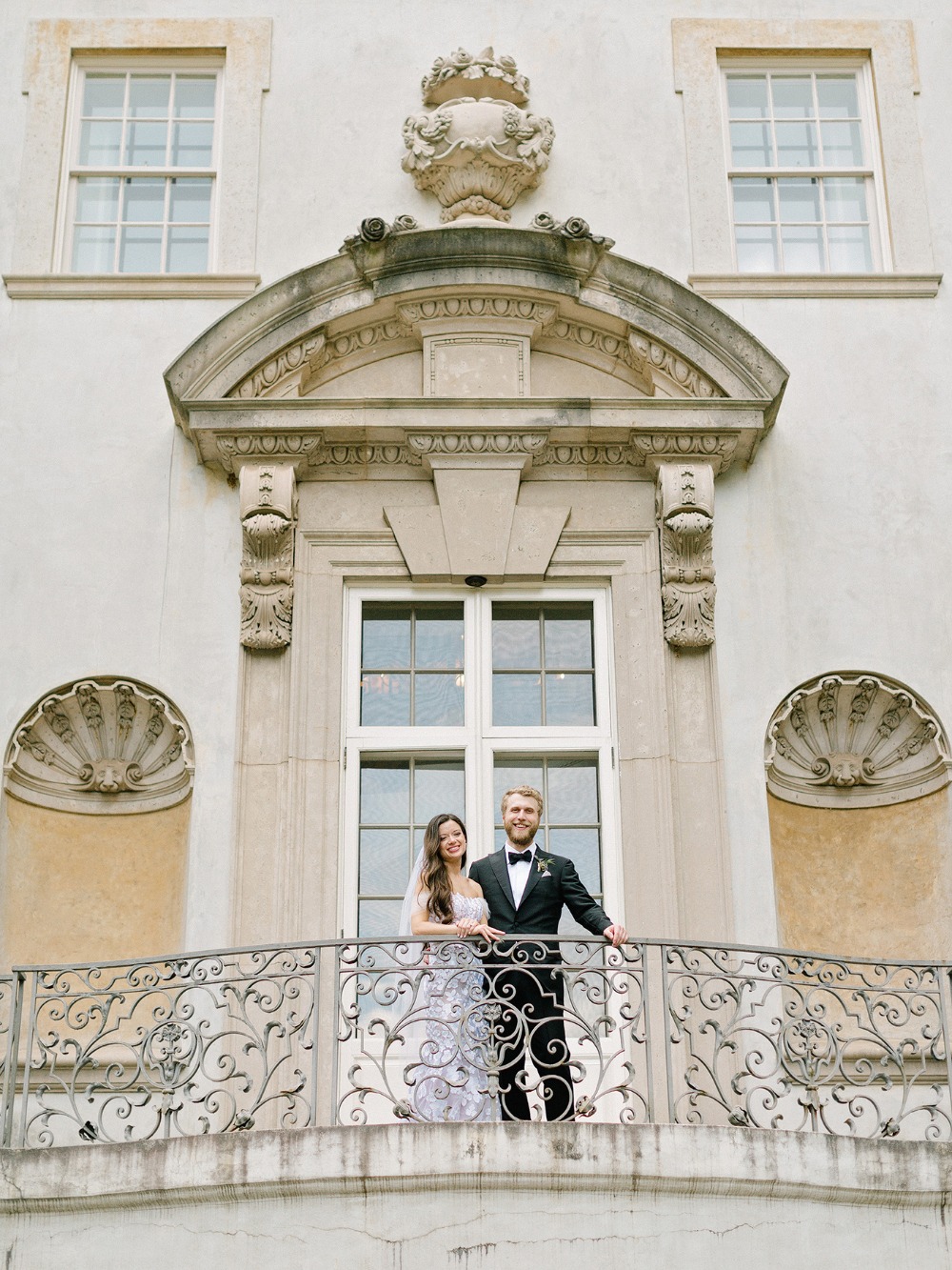 Newlyweds pose on ornate balcony for wedding photos