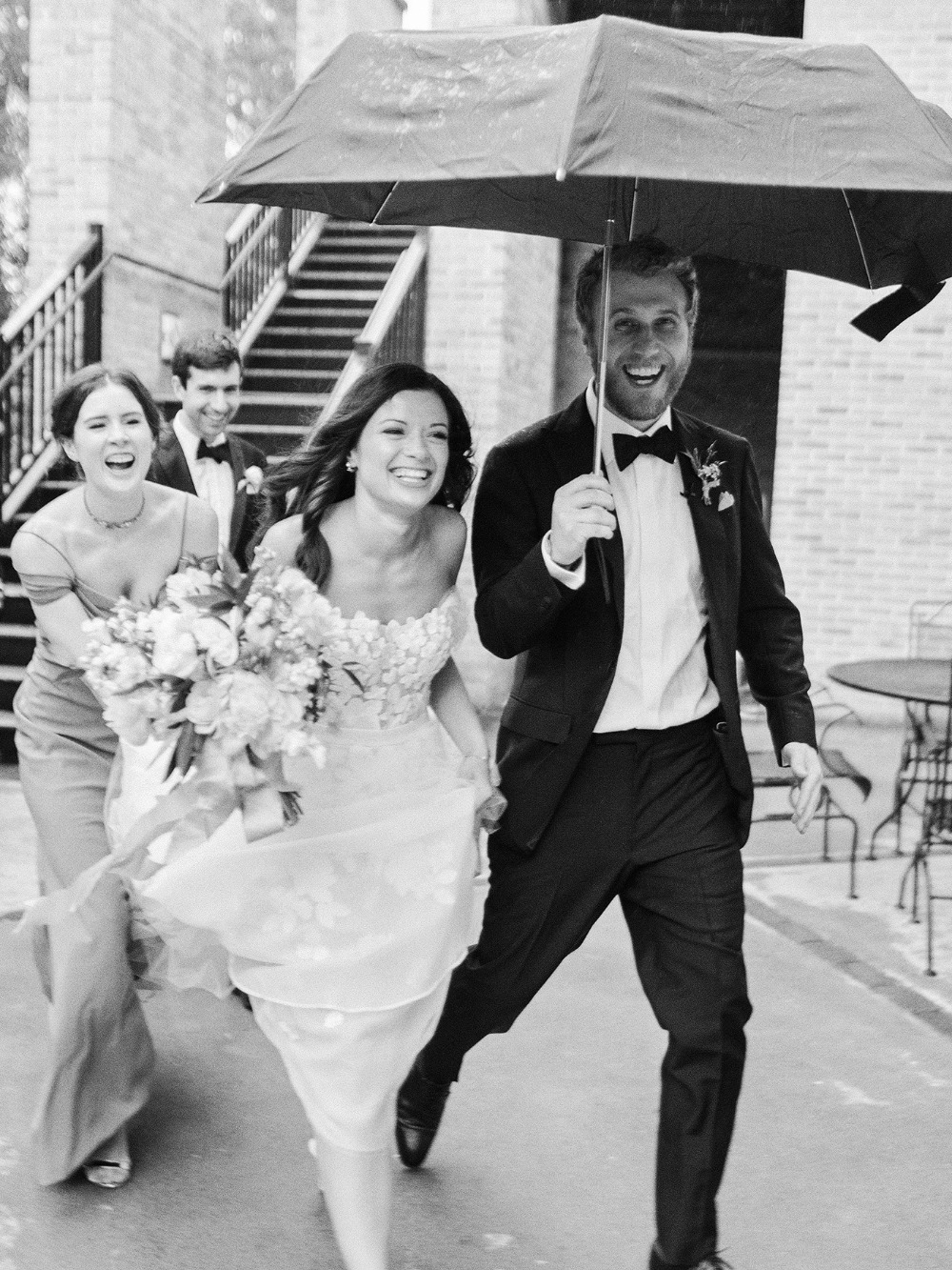 Joyful wedding party running under an umbrella in the rain