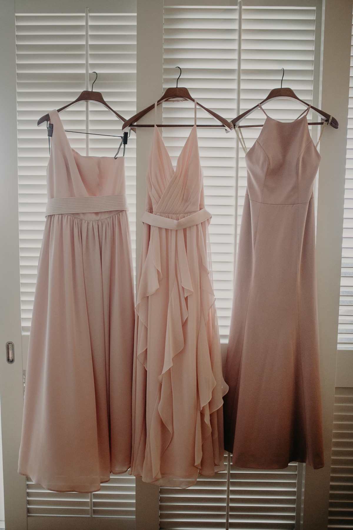 Three elegant pink bridesmaid dresses hanging in a row