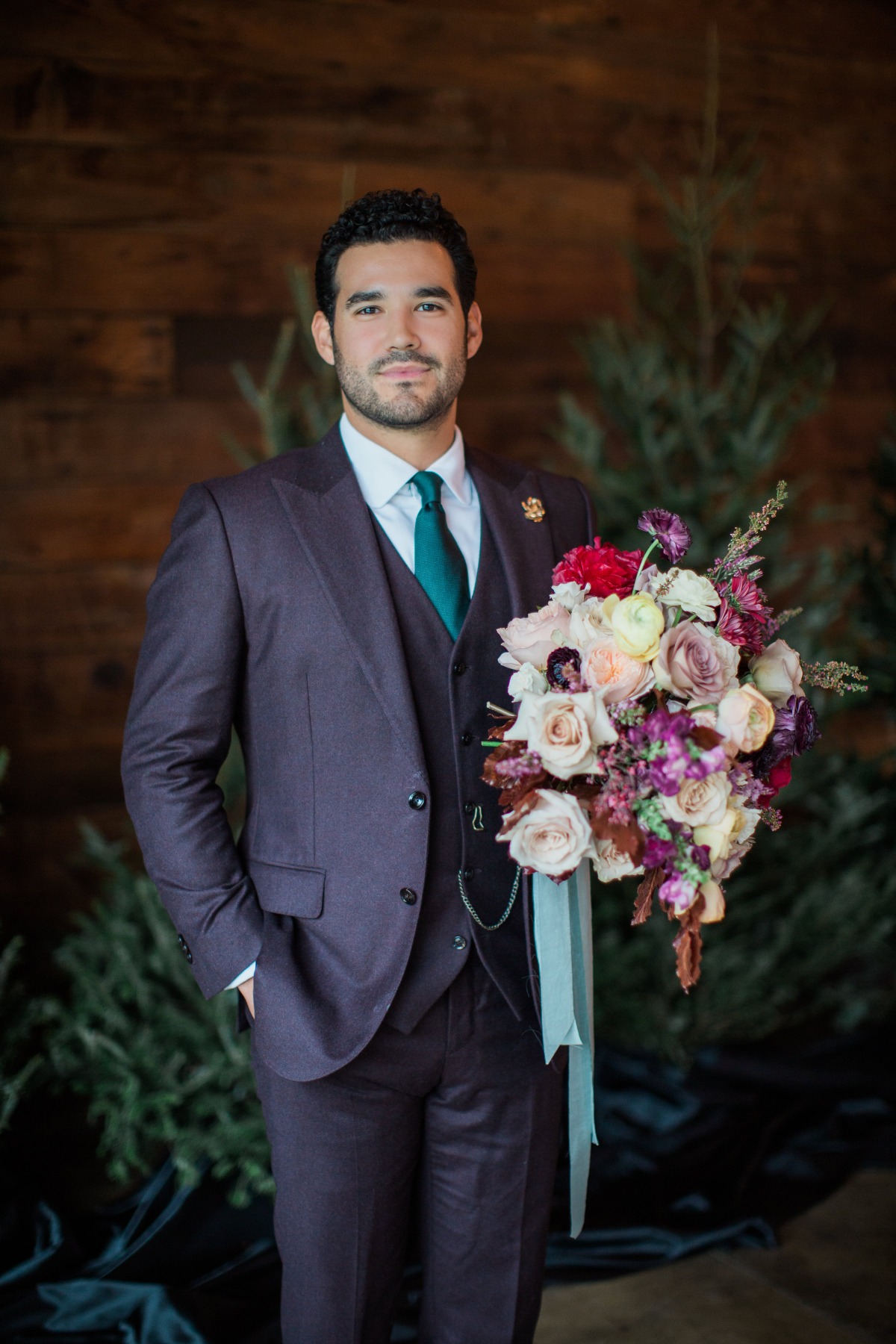 Groom in a purple suit holding a wedding bouquet, looking at the camera