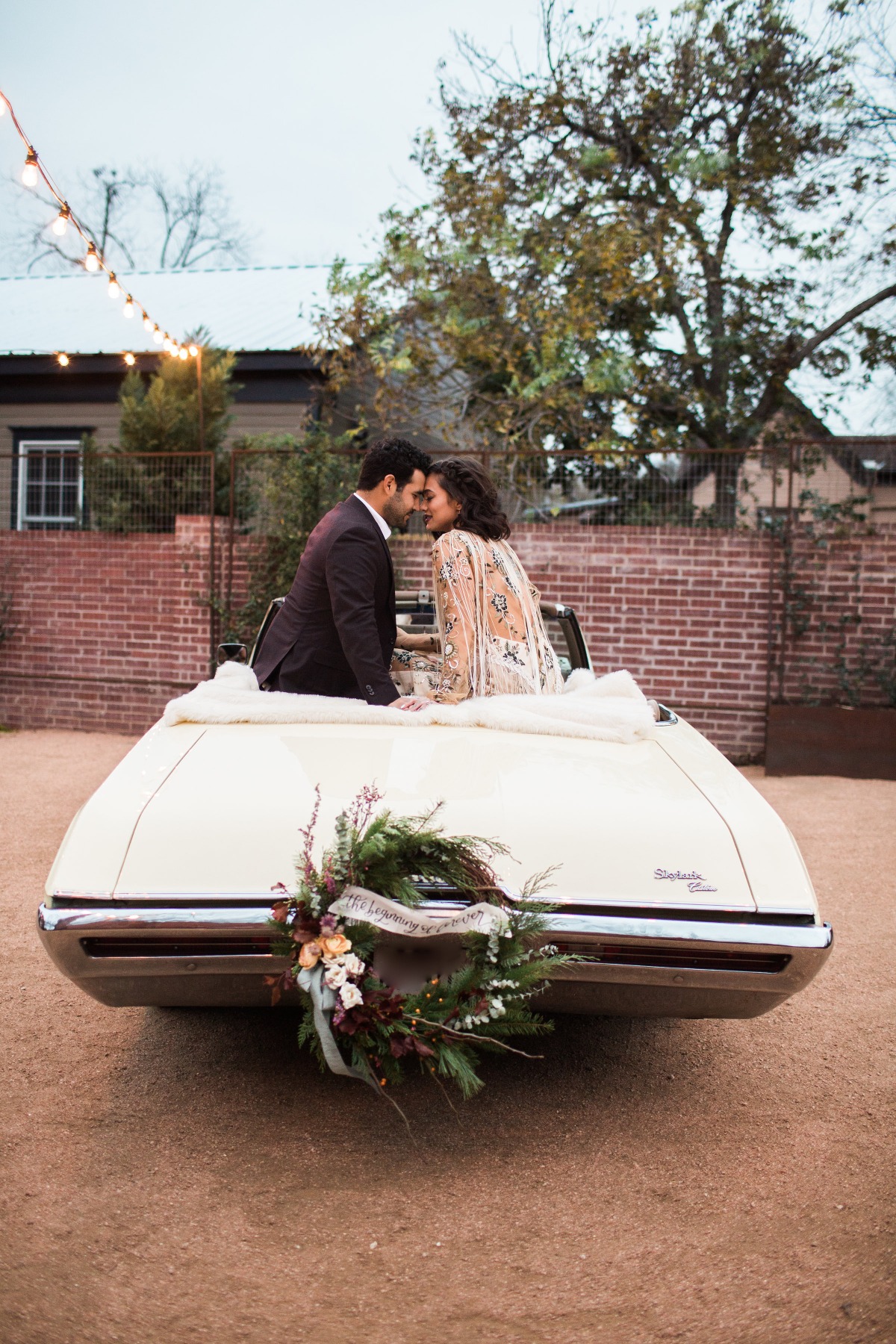 Newlyweds share a tender moment over a vintage car with festive decor