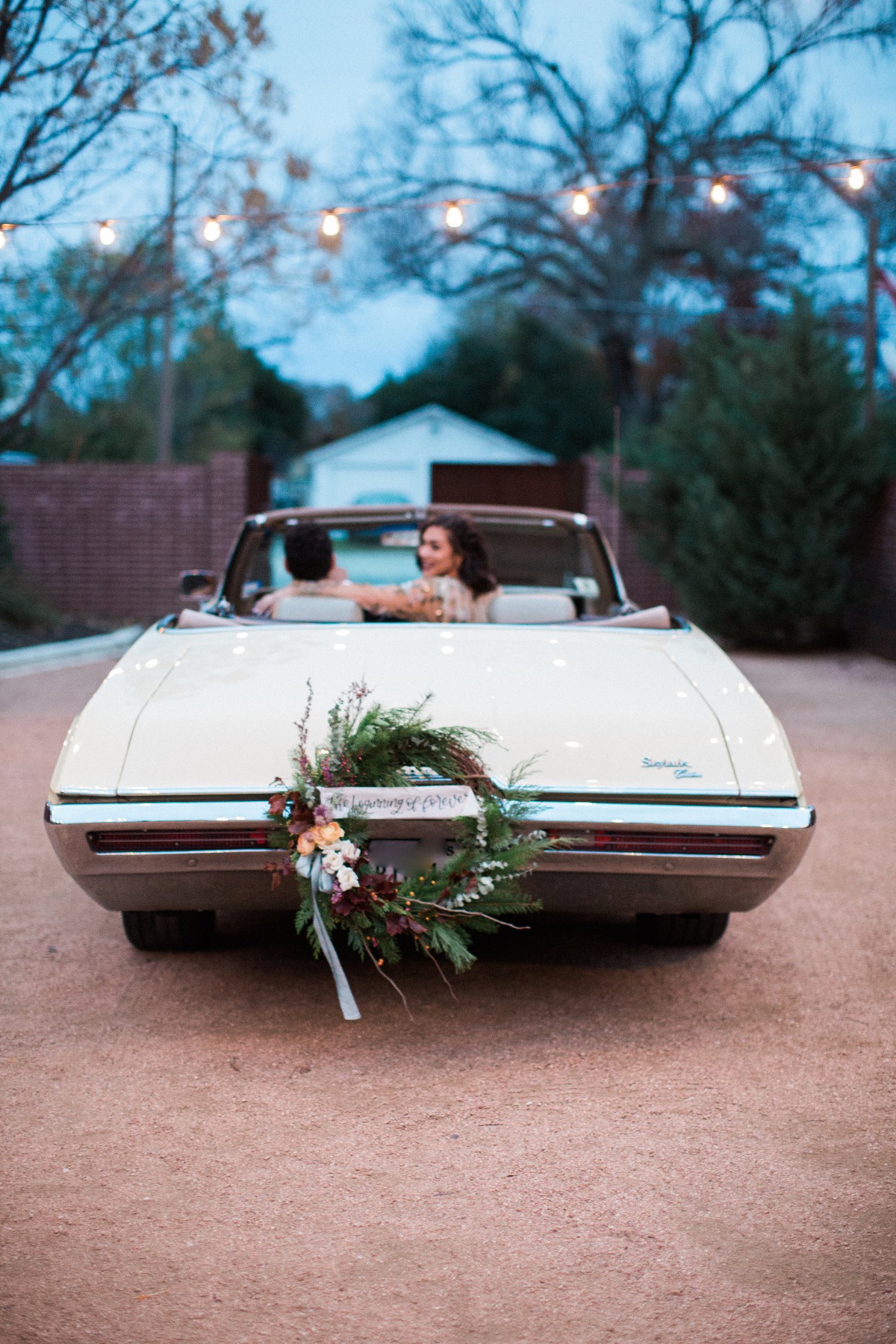 Newlyweds driving off in a classic convertible car with floral decor