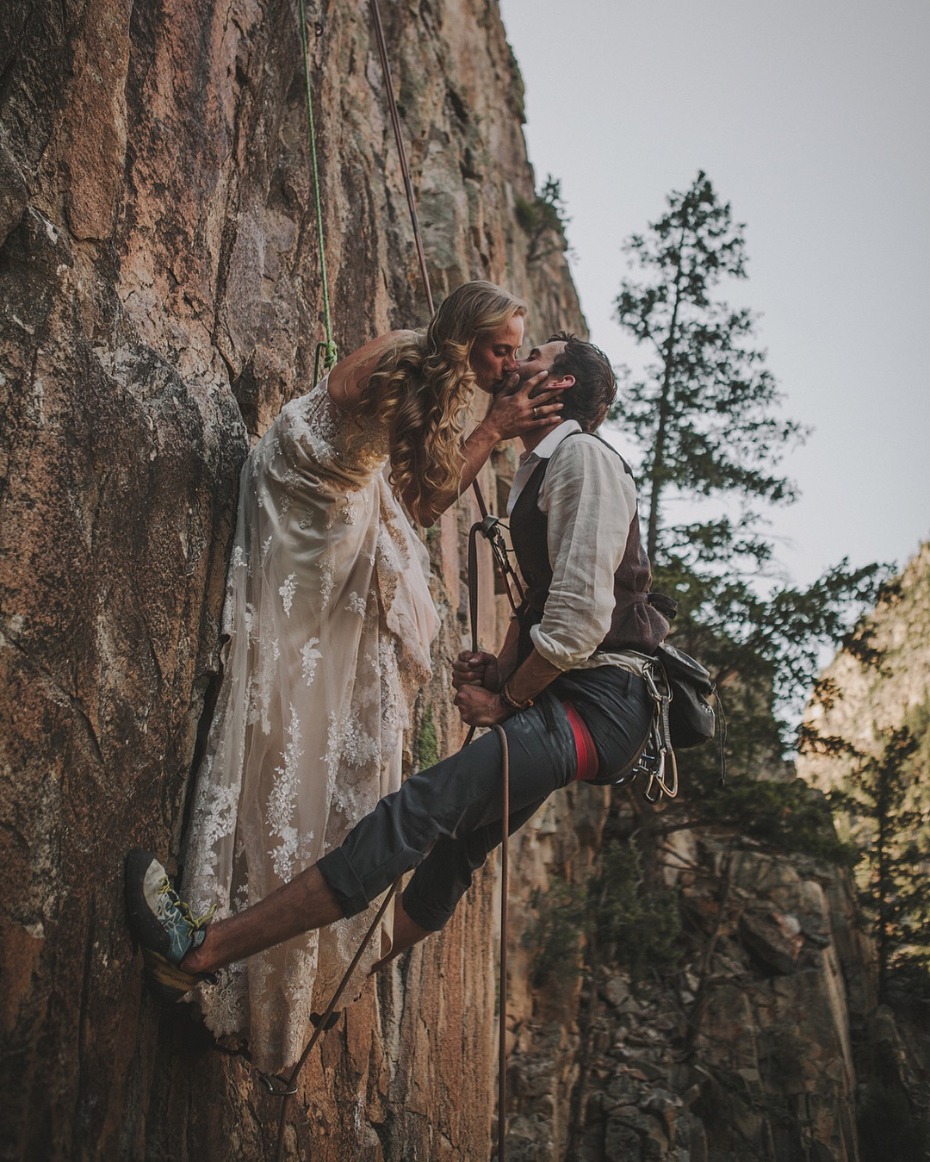 Bride and groom rock climbing with dress and suit on
