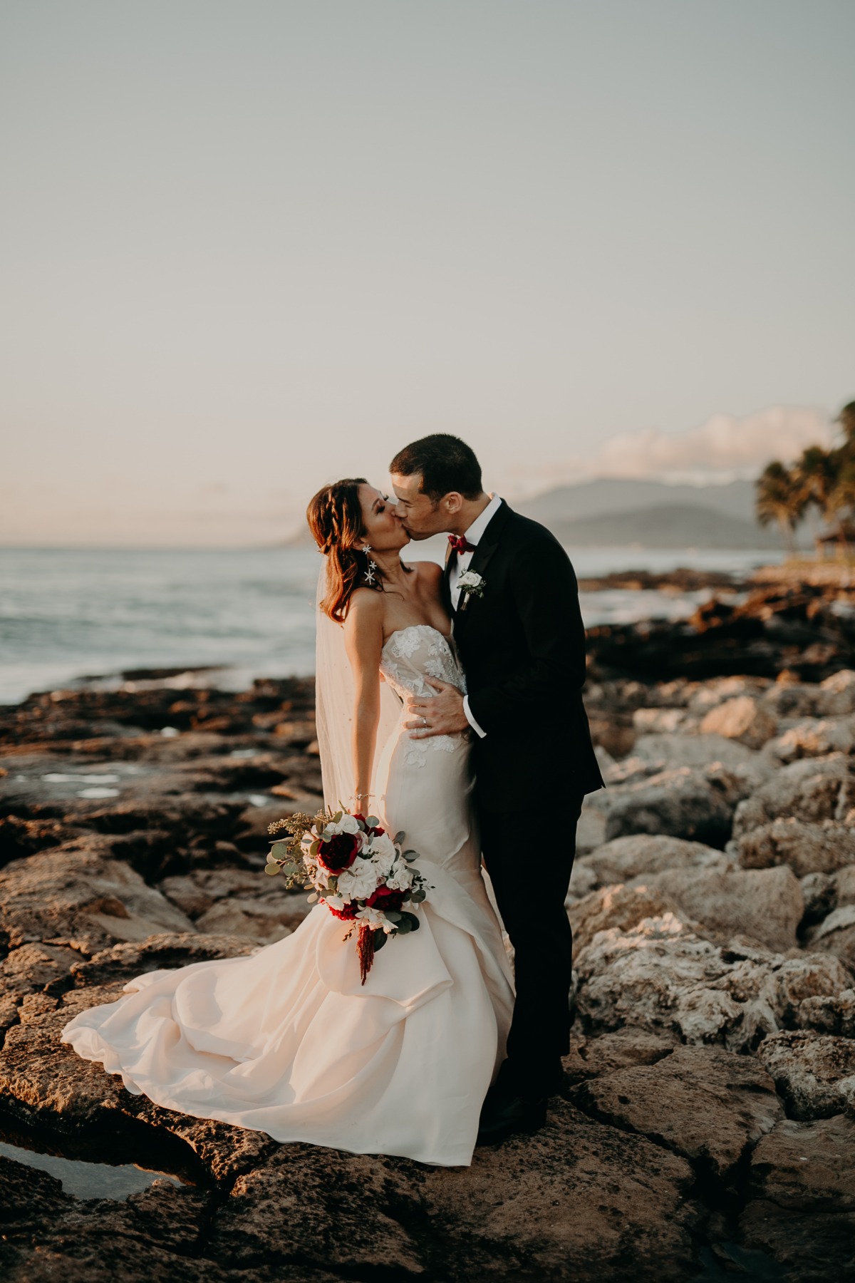 Bride and groom kissing on the rocks at sunset beach wedding