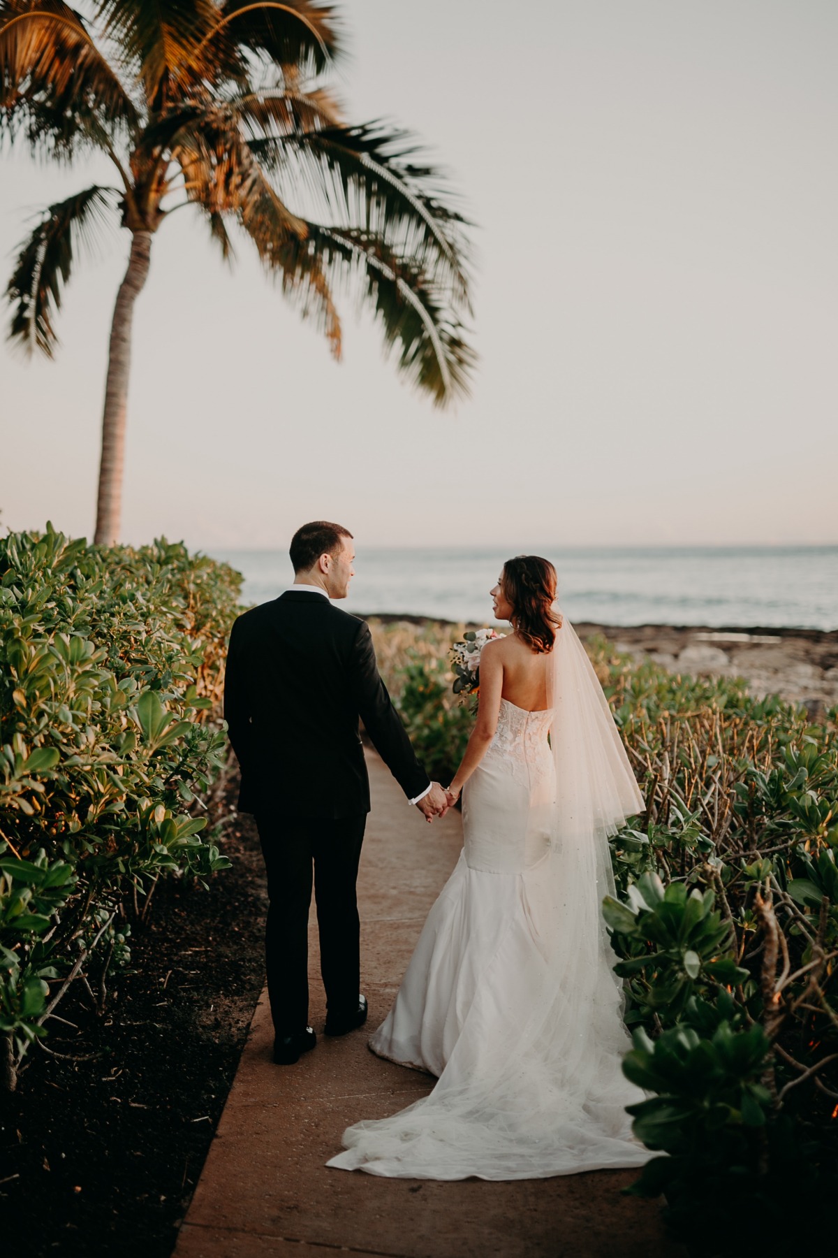 Newlyweds holding hands on a path to the ocean, romantic destination wedding
