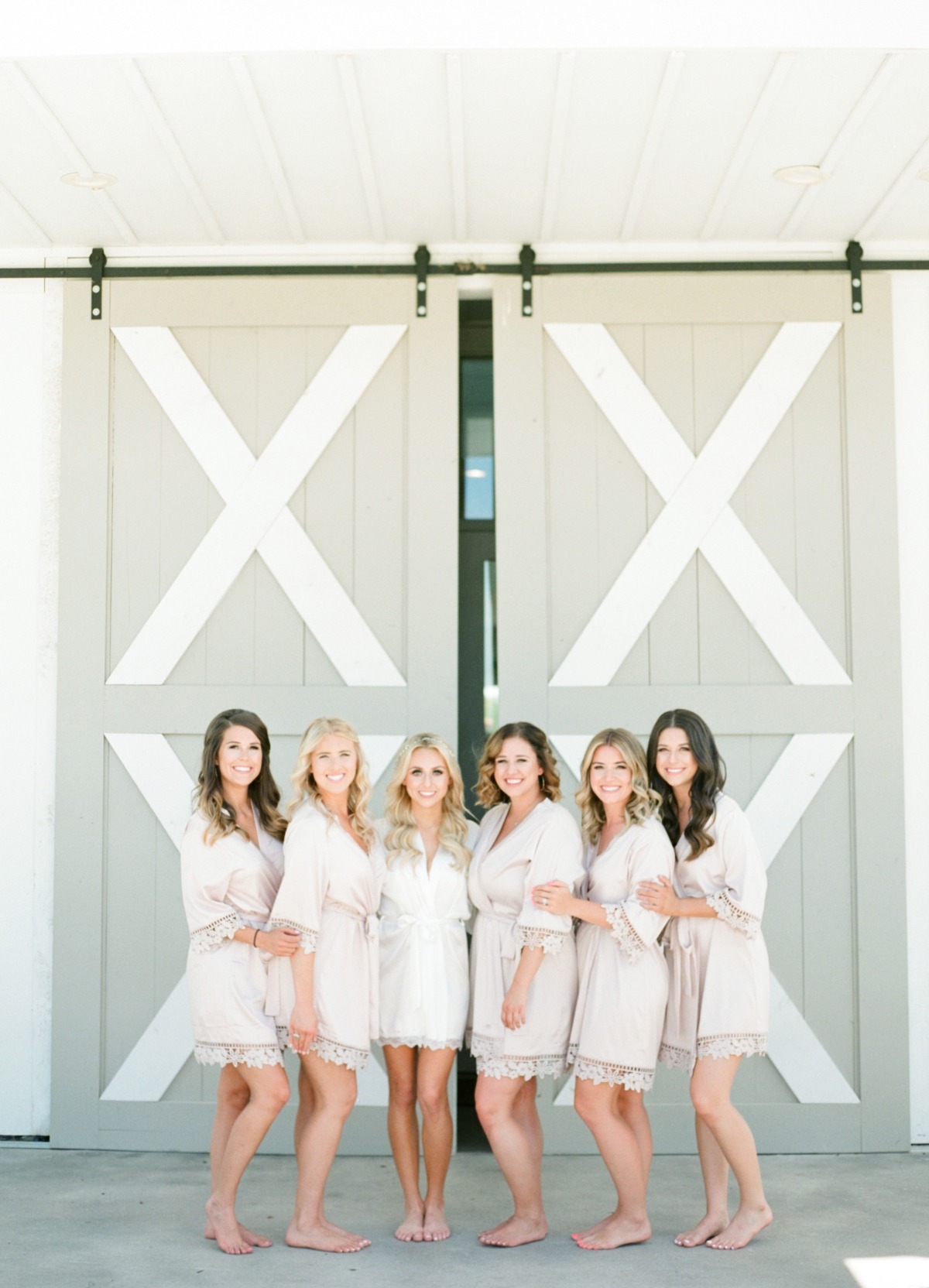 Bridesmaids in robes pose in front of a barn door on a wedding day