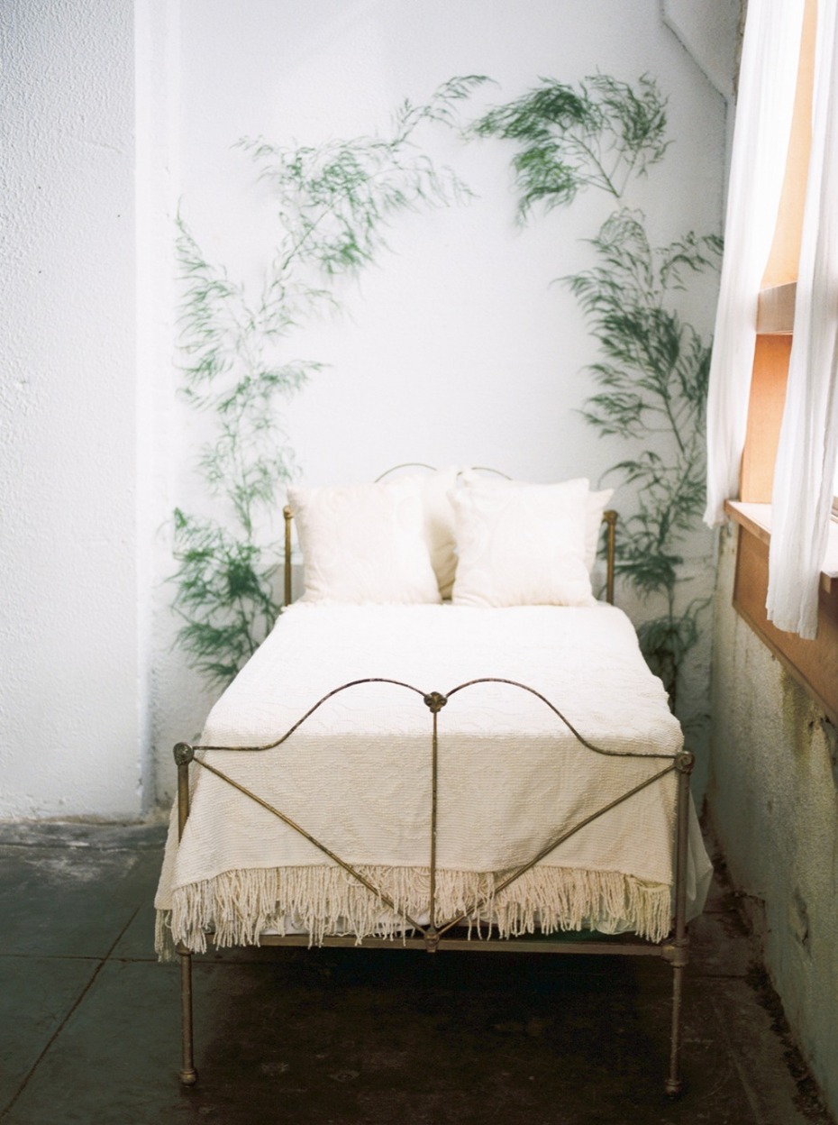 Metal bed with white bedding against a leafy wall